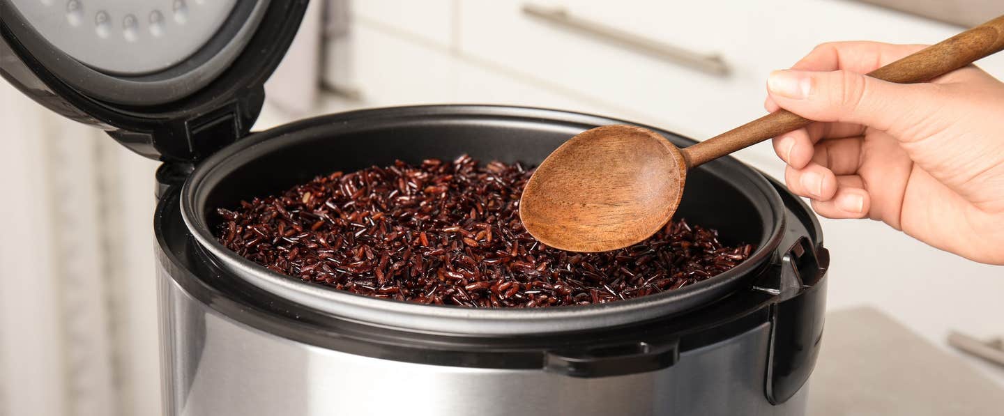 A woman's hand holding a spoon reaches into an instant pot full of wild rice