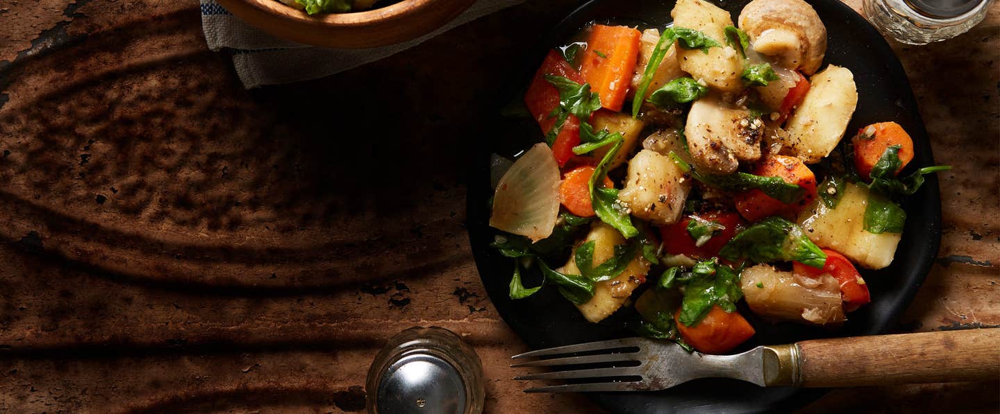 A black plate of Jerk-Seasoned Veggies with Yuca with a wooden-handled fork resting in the plate