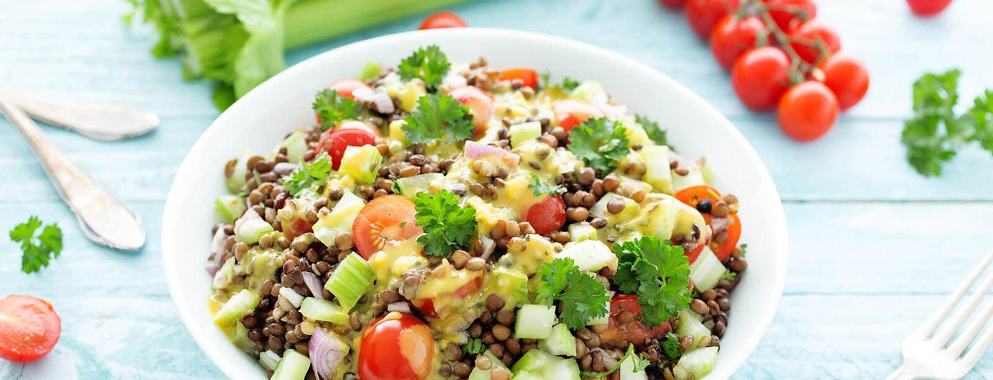 French Green Lentil Salad on a pale blue wooden table with fresh tomatoes, celery, and parsley