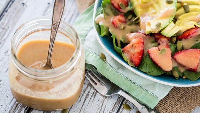 A mason jar of "Magical" Applesauce Vinaigrette next to a salad with fresh strawberries, spinach, and avocado, drizzled with the vinaigrette