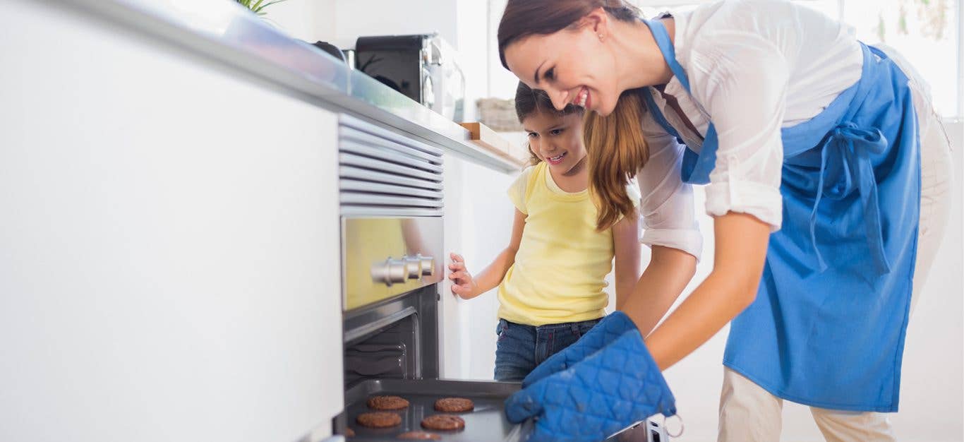 mother and child taking baked cookies from oven