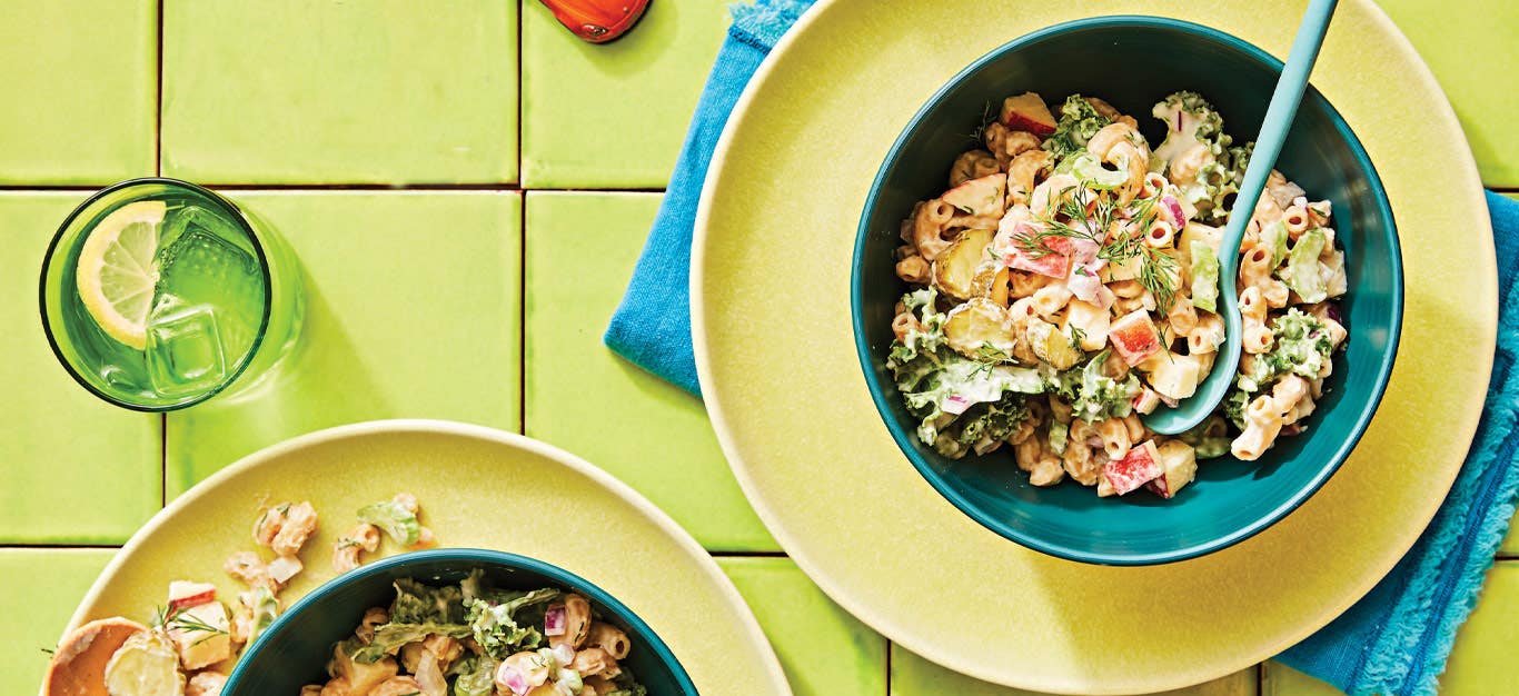 Dilly Vegan Macaroni Salad in a blue bowl on a yellow plate against a green tile background