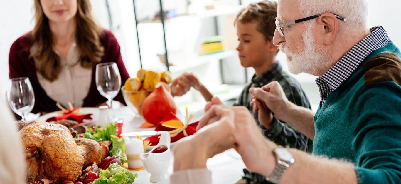 Multiple generations of a family gathered around a not plant-based holiday meal saying grace