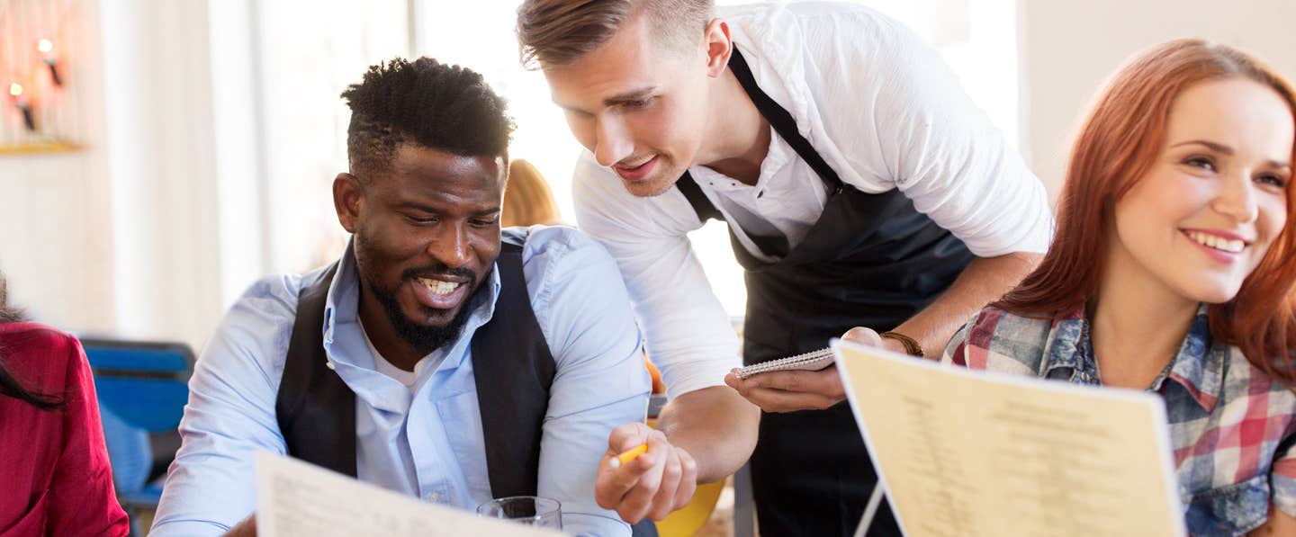 A young man and a woman at a restaurant, the man is talking to waiter, asking about the menu