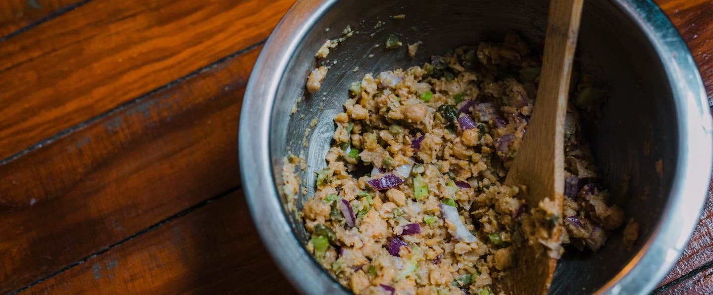 A dark grey ceramic bowl of vegan tuna salad with a small wooden spoon in the bowl