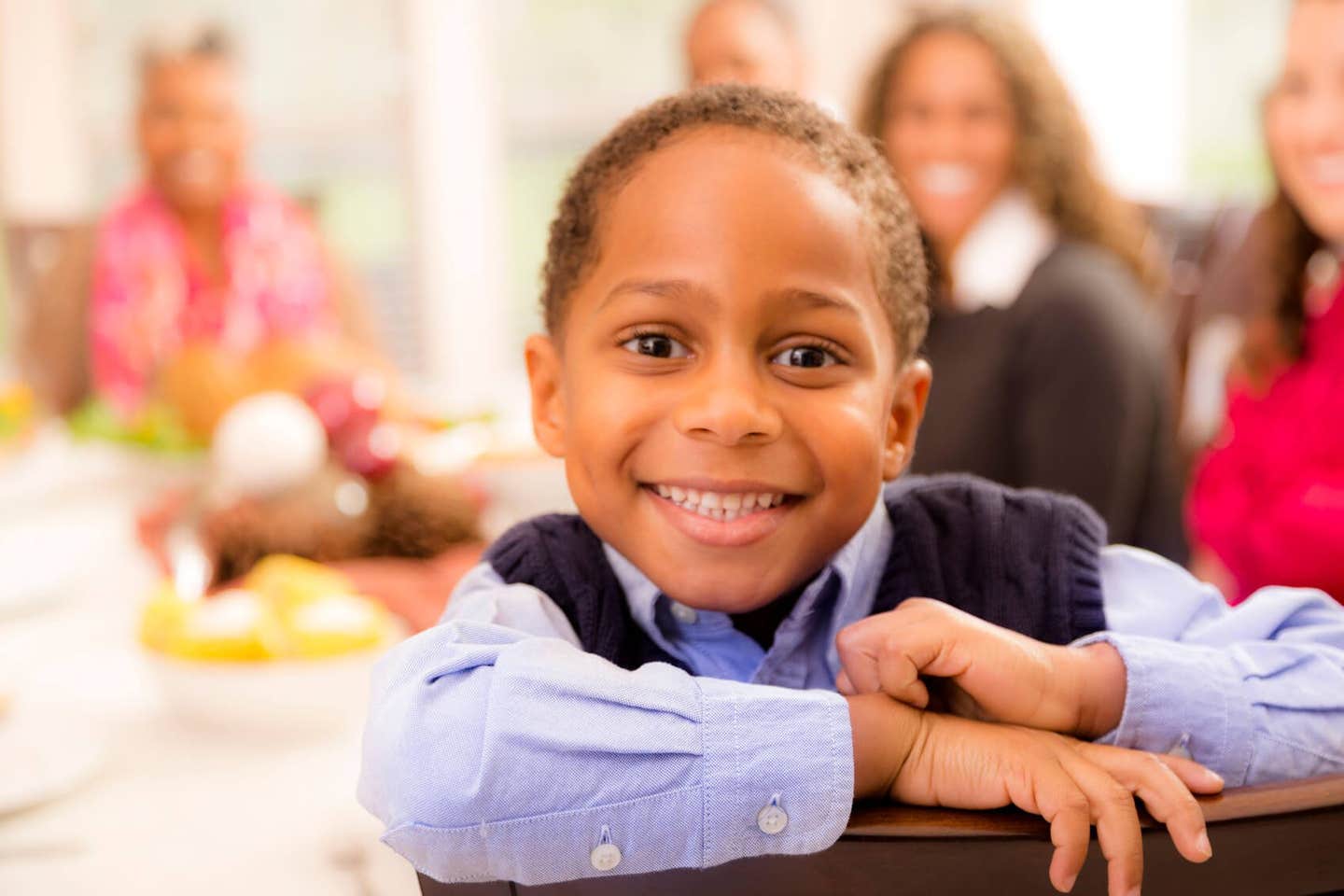 Young boy with his family in the background, looking into the camera with a big smile