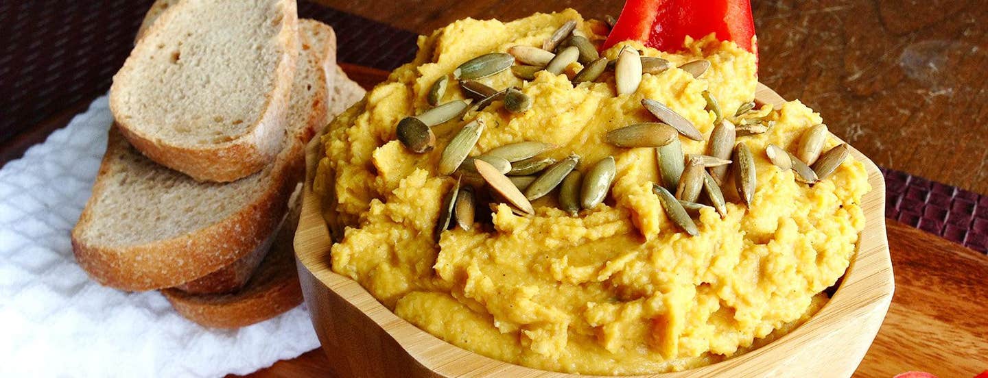 Pumpkin Hummus in a wooden bowl next to slices of crusty whole grain bread