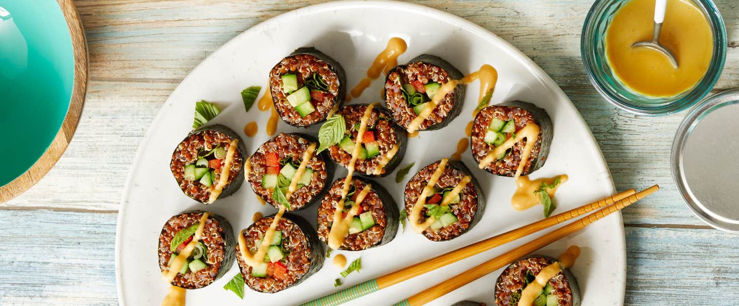 quinoa sushi rolls on a white plate, drizzled with thai peanut sauce, two chopsticks set on the plate