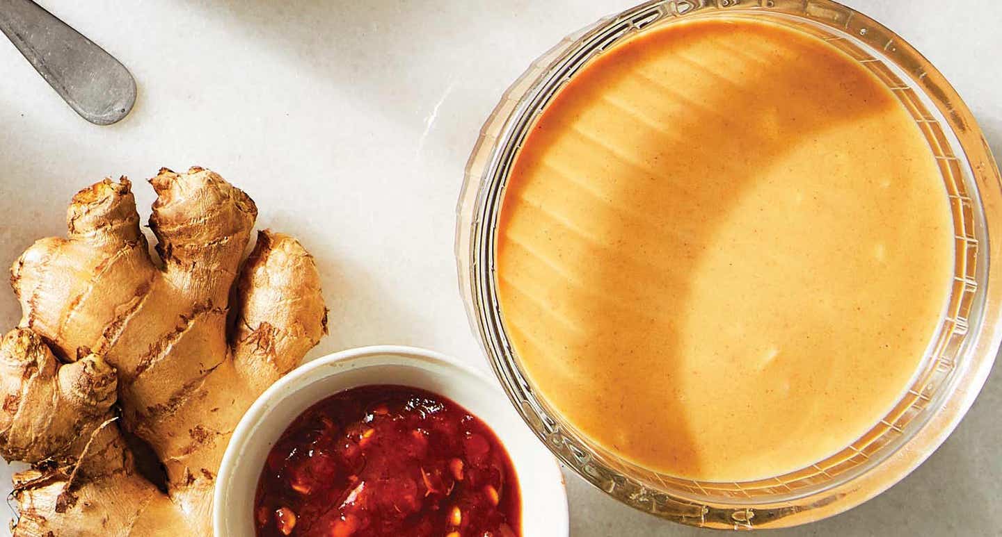 A bowl of oil-free peanut dressing shown beside two ingredients (a knob of fresh ginger and a small ramekin of chili paste)