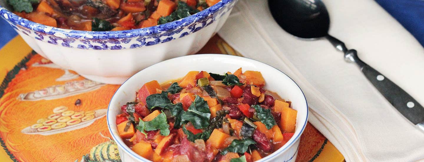 A smaller white bowl of Sweet Potato Chili with Kale next to a larger bowl and a spoon and napkin