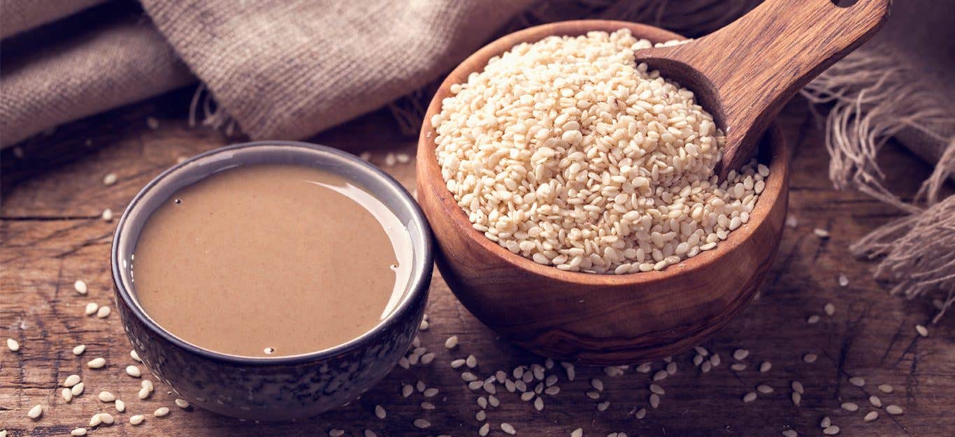 A small bowl of tahini next to a larger wooden bowl of sesame seeds.