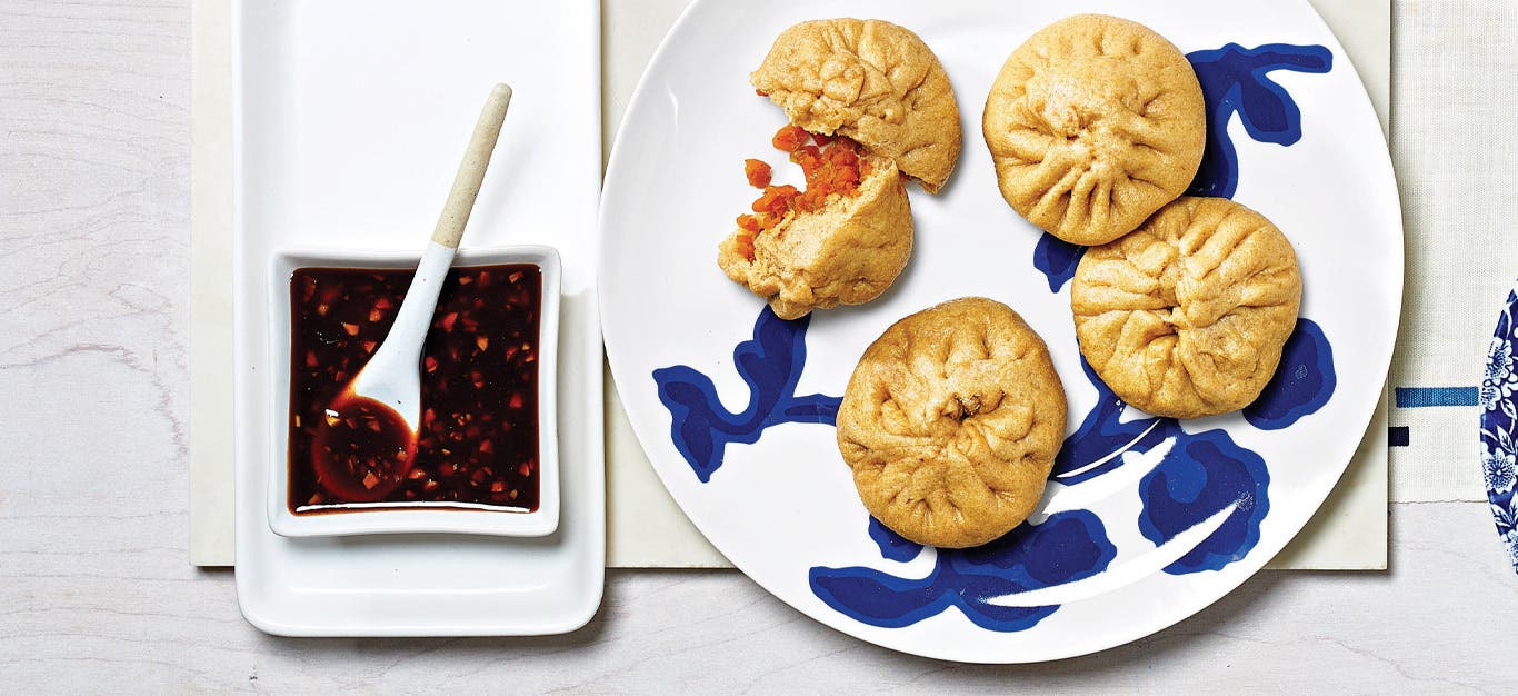 Hannah Che’s Vegan Bao Buns on a blue and white china plate next to a square dish of spicy soy dipping sauce