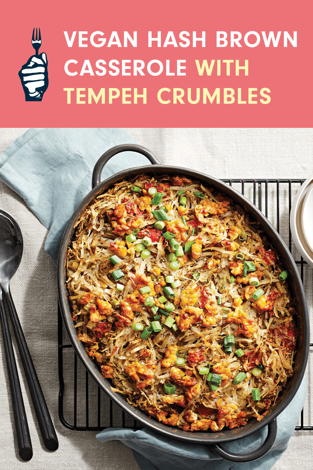 A large casserole dish of Vegan Hash Brown Casserole with Tempeh Crumbles on a wire cooling rack next to metal serving spoons.