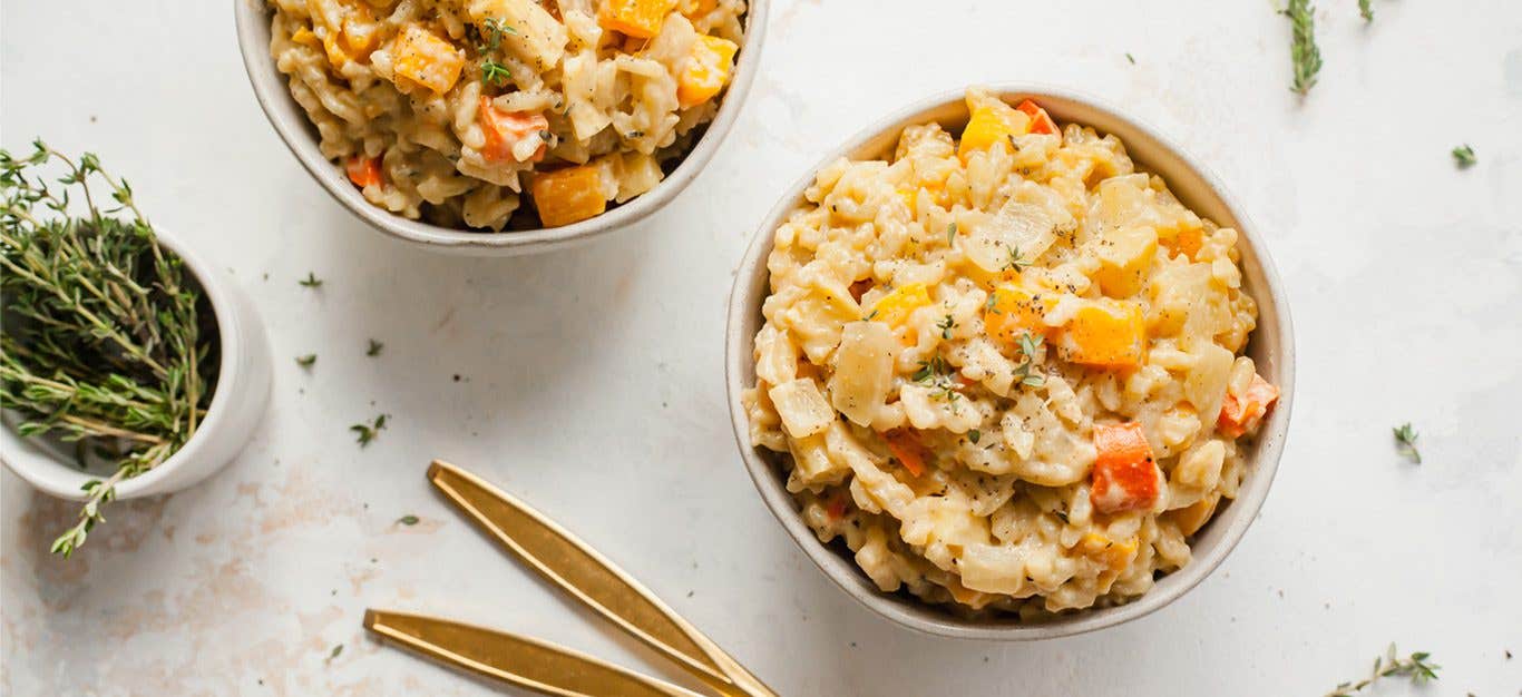 Two bowls of winter vegetable vegan risotto next to a small pot of fresh rosemary stalks