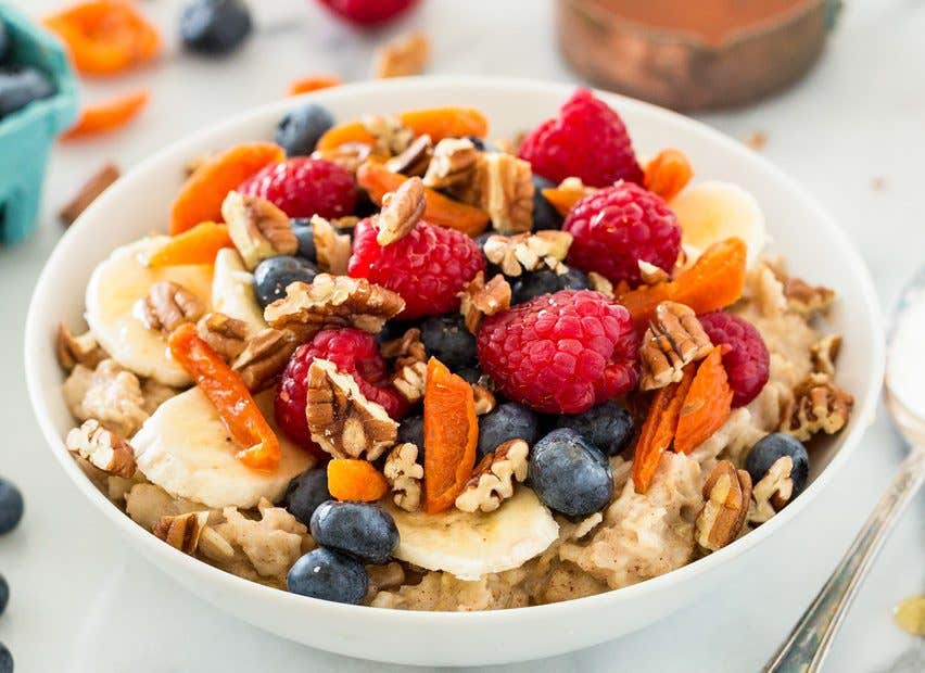 A healthy bowl of oatmeal with raspberries, blueberries, banana slices, and walnuts