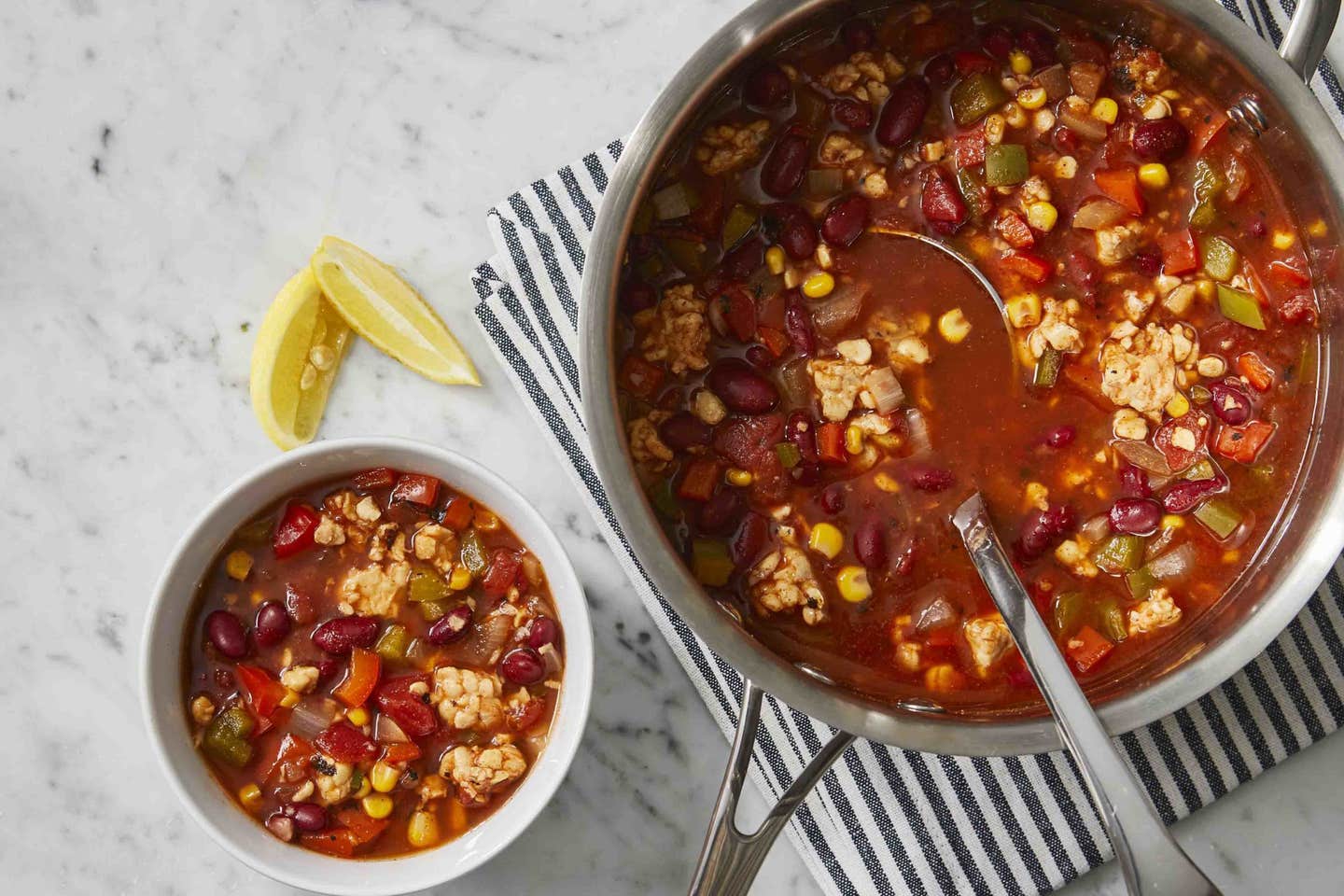 A pot of vegan tempeh chili next to a bowl of the chili with some lemon slices on the side