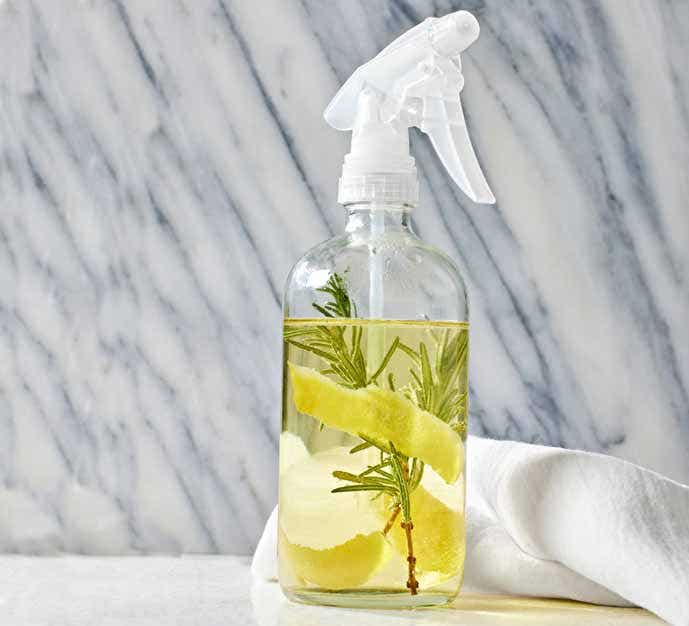 vinegar cleaner with strips of lemon peel and rosemary in a clear spray bottle 