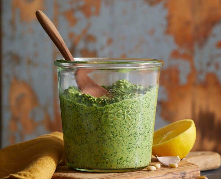 carrot top pesto in a glass jar with a wooden spoon